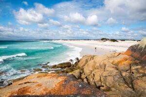 Pristine white sand beach meets clear turquoise sea at Bay of Fires with orange rocks in foreground